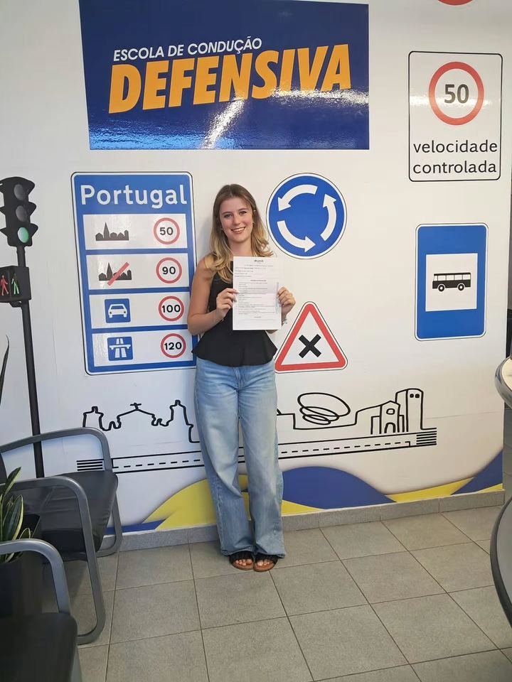 Nova condutora a mostrar o resultado do exame em frente à parede de sinais da escola